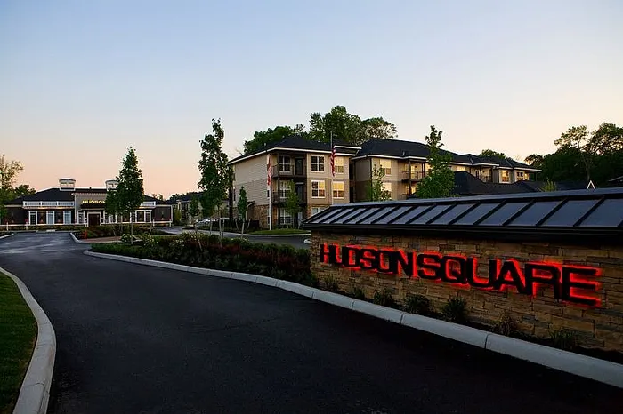 Elegant exterior view of Hudson Square apartments with modern architecture, lush greenery, and warm evening lighting.