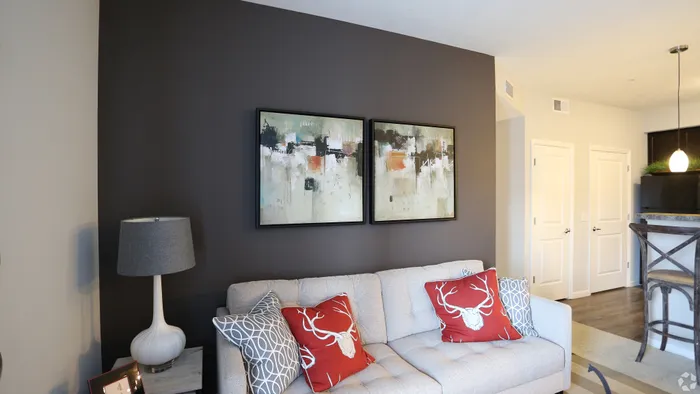 Modern living room with stylish artwork, cozy gray couch, and vibrant red accent pillows, offering a welcoming and chic atmosphere.