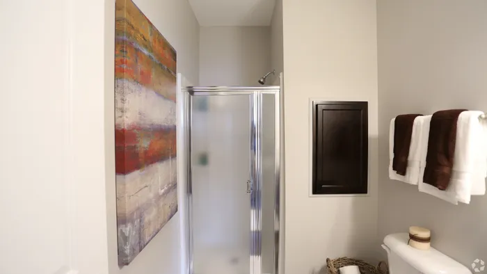 Elegant bathroom featuring a modern glass shower, abstract wall art, and neatly displayed towels for a luxurious touch.