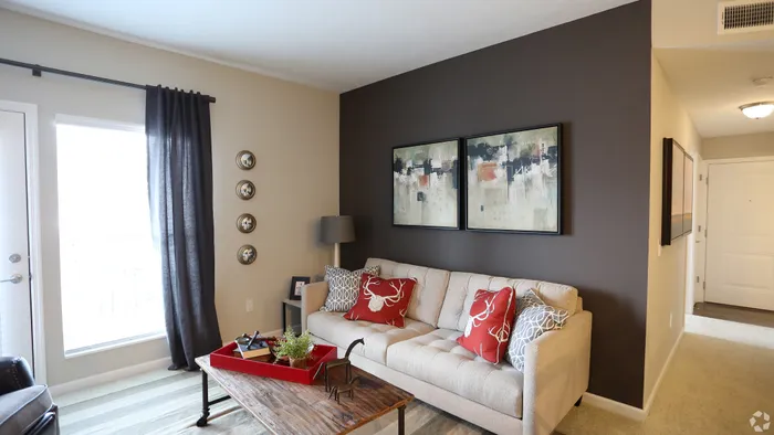 Chic living room with a cozy beige sofa, vibrant red deer-themed cushions, contemporary artwork, and a rustic coffee table, offering a stylish and inviting atmosphere.
