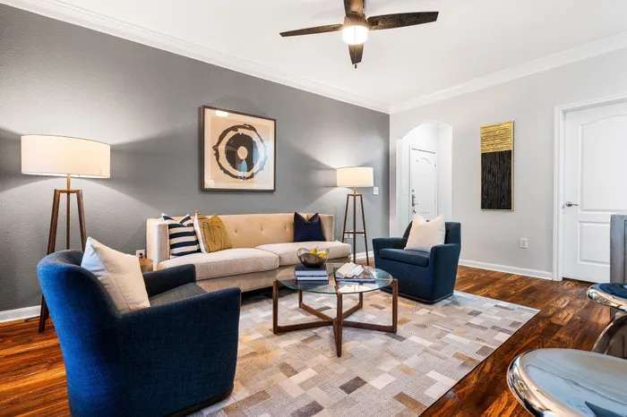 Contemporary living room with elegant decor, featuring plush chairs, a cozy sofa, and modern artwork, complemented by stylish lighting and a chic glass coffee table.