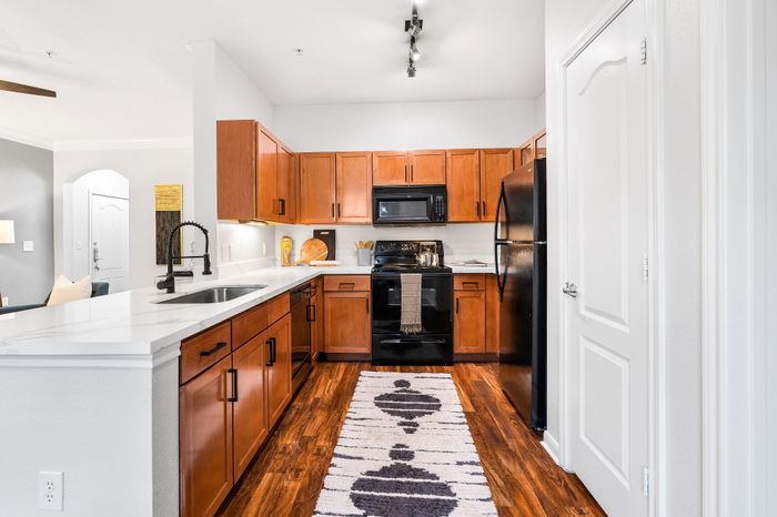 Sleek modern kitchen with warm wood cabinetry, stylish appliances, and elegant white countertops in a bright, open apartment layout.
