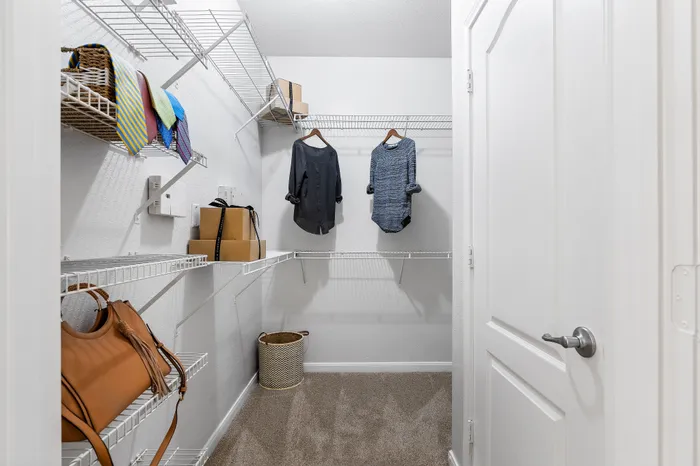 Spacious walk-in closet with sleek white shelving, hanging outfits, and organized storage boxes.