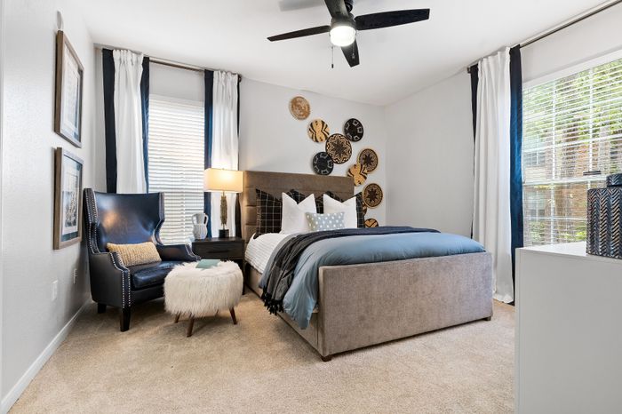 Cozy, stylish bedroom with plush bedding, elegant accent chair, and chic wall decor, bathed in natural light.
