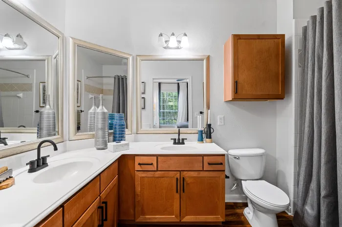 Modern and bright bathroom featuring wooden cabinets, sleek countertop, large mirrors, and elegant decor accents.