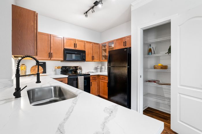 Modern kitchen with sleek marble countertops, stylish black appliances, and elegant wooden cabinetry, featuring a spacious pantry.