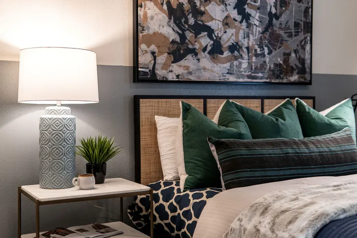 Cozy bedroom scene with stylish patterned bedding, plush green throw pillows, and a modern bedside table featuring a chic lamp and vibrant plant.