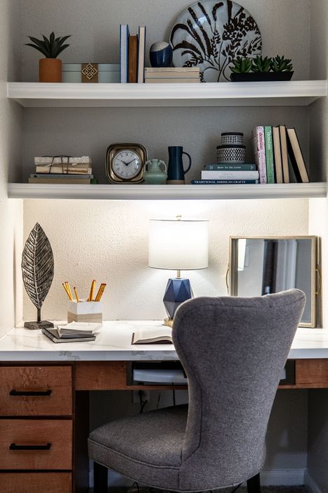 Chic and cozy home office nook featuring a stylish gray chair, elegant desk accessories, and artful decor on shelves, perfect for inspiring productivity and creativity.