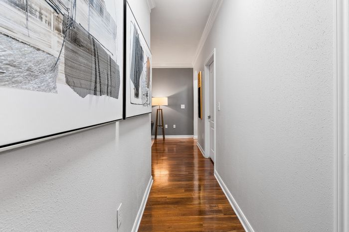 Modern hallway with elegant wooden flooring, contemporary artwork, and a sleek floor lamp providing a warm ambiance.
