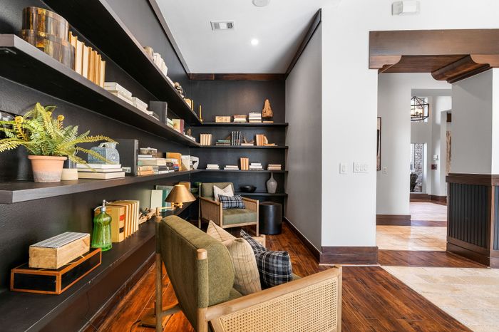 Elegant home library with dark wood shelves filled with books and decor, cozy seating area with green armchairs, and warm wood flooring.