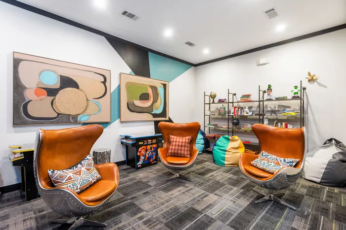 Vibrant and contemporary apartment lounge featuring modern leather chairs, abstract art, and a stylish bookshelf with colorful decor.