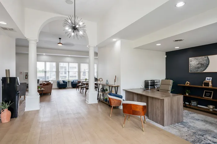 Elegant modern living space featuring sleek office setup and cozy seating under a stylish ceiling light, with abundant natural light and contemporary decor.