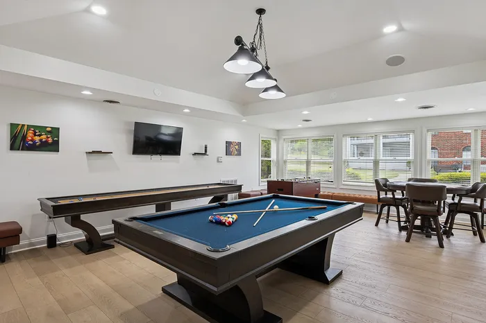 Elegant game room showcasing a stylish billiards table, modern shuffleboard, and cozy seating area with large windows for natural light.