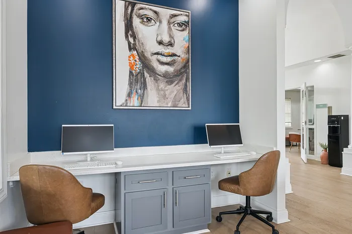 Chic workspace area with modern computers, stylish brown chairs, and captivating artwork on a rich blue accent wall, perfect for productivity and creativity.