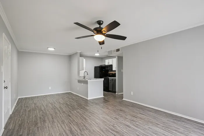 Modern open-concept living space featuring sleek hardwood floors, a ceiling fan, and a contemporary kitchen with granite countertops.