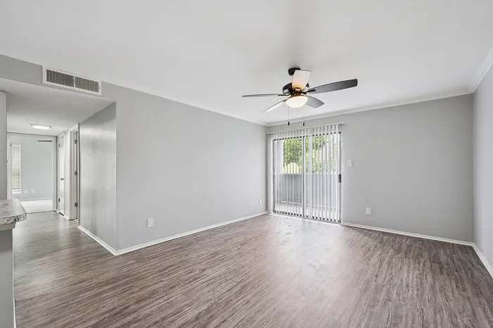 Bright living room with sleek wood flooring, large sliding glass doors to a balcony, and a modern ceiling fan.