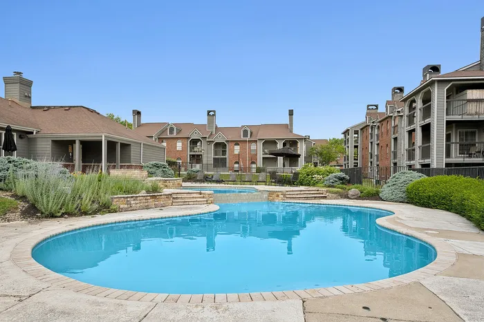 Elegant apartment complex with charming architecture, featuring a sparkling blue swimming pool surrounded by lush landscaping.