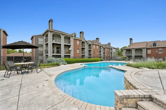 Charming apartment complex featuring a pristine swimming pool, surrounded by modern brick buildings and cozy outdoor seating.
