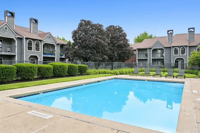 Charming apartment complex with modern architecture overlooking a sparkling pool, surrounded by lush greenery and inviting deck chairs.