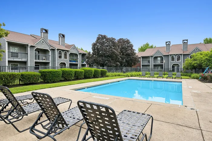 Inviting apartment complex featuring charming architecture with a sparkling outdoor pool and relaxing lounge chairs, set amidst lush greenery.
