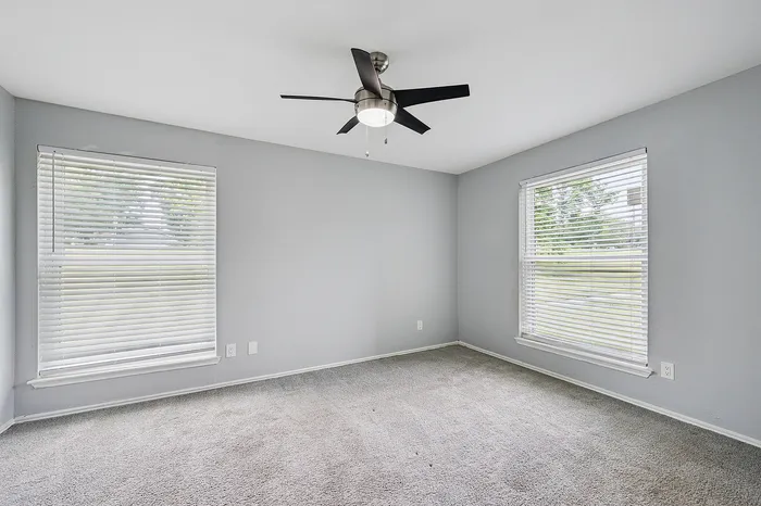 Bright and spacious bedroom with plush carpeting, large windows, and a modern ceiling fan for ultimate comfort.