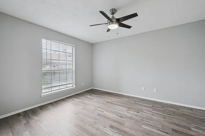 Bright and airy room featuring sleek hardwood flooring, modern ceiling fan, and large window with blinds for ample natural light.