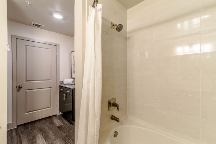 Modern bathroom featuring a sleek bathtub with shower, elegant tiled walls, and stylish dark wood flooring.