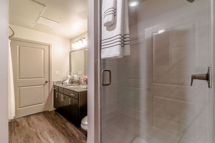 Modern bathroom with elegant glass shower, stylish wooden flooring, and sleek granite countertop for a luxurious feel.