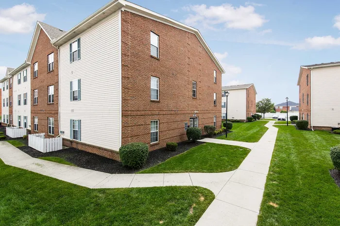 Charming brick apartment complex with well-maintained green lawns, inviting pathways, and bright windows under a clear blue sky.