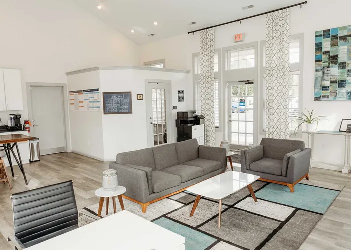 Bright and modern communal area featuring sleek gray sofas, a stylish white coffee table, and contemporary decor with large windows enhancing natural light.