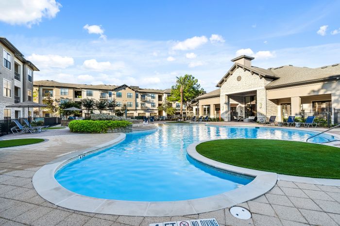 Luxurious apartment complex featuring a sparkling pool, modern architecture, and ample lounge seating.