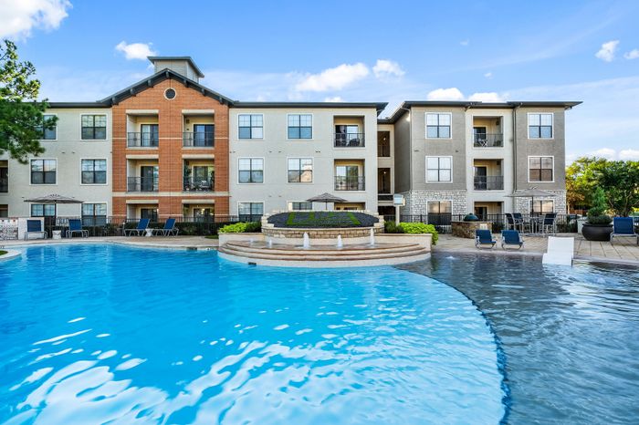 Elegant apartment complex with a stunning resort-style pool, surrounded by palm trees and modern architecture, perfect for luxurious living.