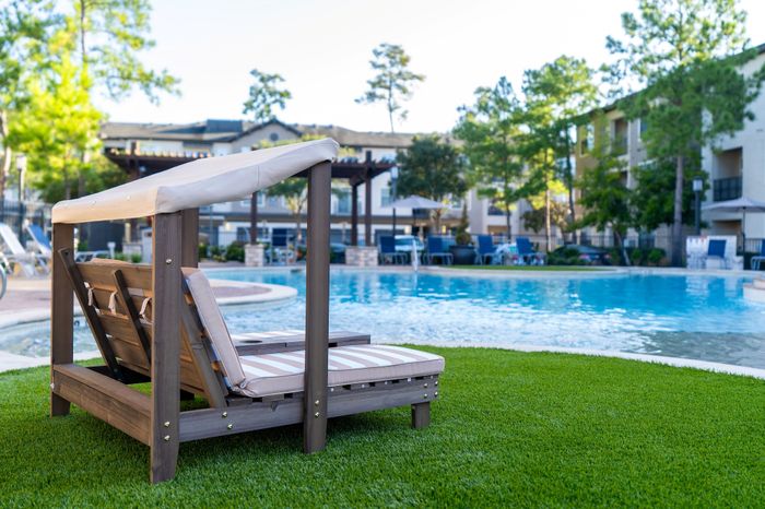 Luxurious poolside retreat featuring elegant lounge chairs surrounded by lush greenery and modern apartment buildings in the background.
