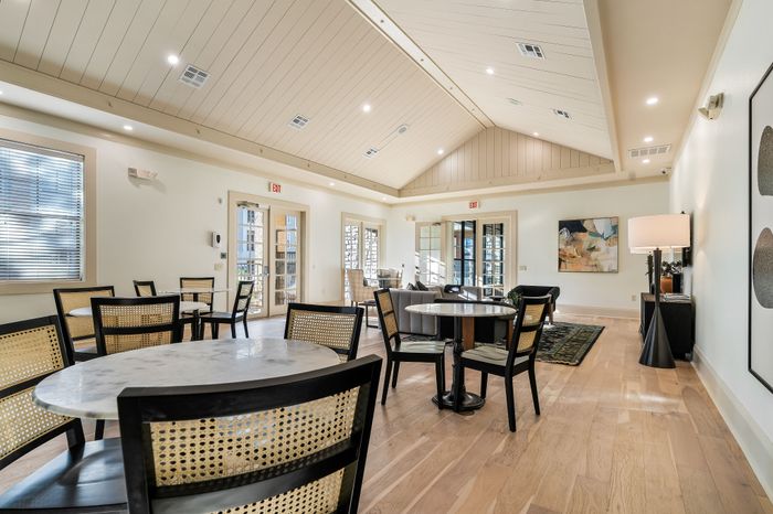 Bright and inviting community room with elegant wood flooring, modern dining tables, and expansive windows for natural light.