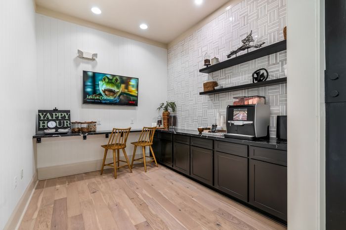 Chic apartment kitchen corner with elegant black cabinets, modern coffee machine, and inviting bar seating under cozy lighting.