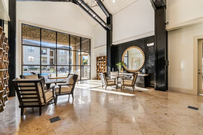Elegant lounge area with high ceilings, large windows, and modern seating overlooking a swimming pool, perfect for relaxation and entertainment.