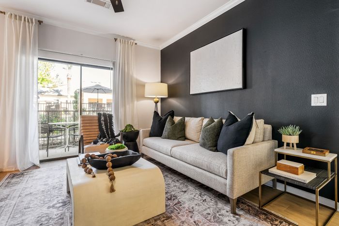 Chic and modern living room with a cozy beige sofa, elegant black accent wall, and bright natural light streaming through large glass doors leading to a private patio.