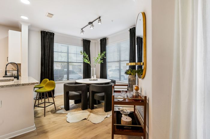 Modern dining area with elegant decor, featuring a round table, stylish chairs, and vibrant greenery, adjacent to a sleek kitchen space with contemporary lighting.
