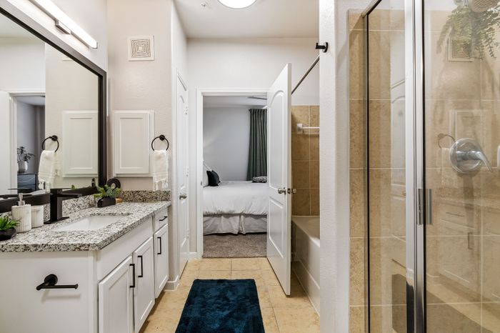 Elegant bathroom featuring a granite countertop, modern fixtures, double doors leading to a cozy bedroom, and a spacious shower.