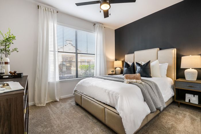 Inviting bedroom with modern decor, featuring a plush bed, chic black accent wall, and warm natural light from large windows.