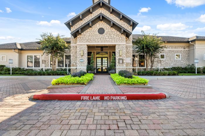 Inviting apartment entrance with lush landscaping and elegant brick facade under a clear blue sky.