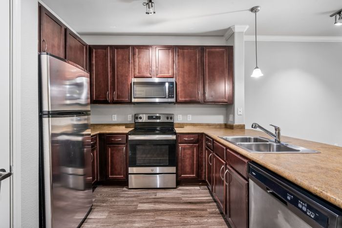 Modern kitchen featuring stainless steel appliances, rich wooden cabinetry, and elegant lighting.