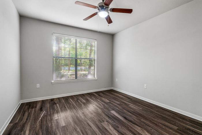 Bright room with elegant wooden floors, large window with blinds, and modern ceiling fan, perfect for personalization.