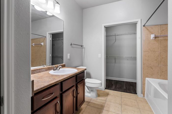 Elegant bathroom featuring a granite countertop, ample cabinet space, and a spacious closet with sleek tile flooring.