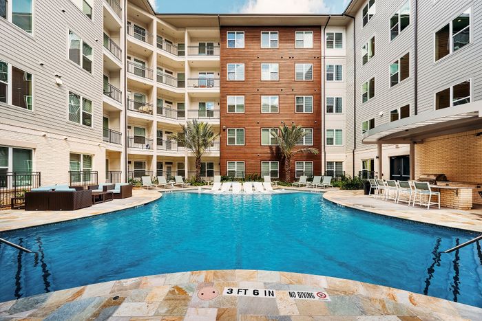 Modern apartment complex with a luxurious pool area, featuring stylish lounge chairs, vibrant palm trees, and inviting outdoor seating for a perfect relaxation spot.
