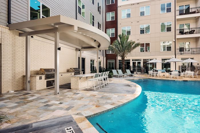 Luxurious apartment complex with sparkling pool, shaded seating, and modern BBQ area for ultimate relaxation.