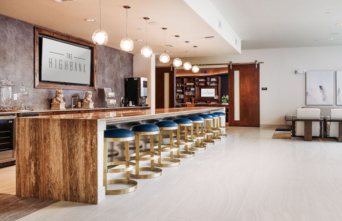 Modern and inviting communal lounge at The Highbank, featuring a sleek bar with stylish blue stools, ambient lighting, and a cozy seating area.