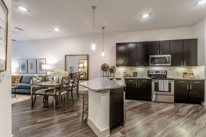 Modern open-concept kitchen and dining area with sleek dark cabinets, granite countertops, and elegant lighting fixtures.