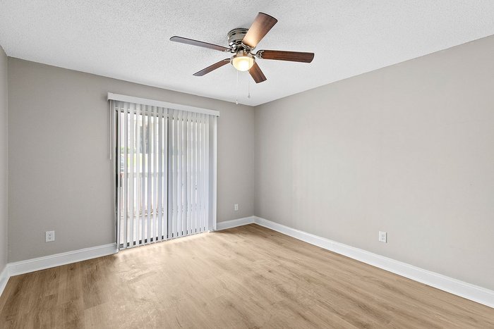 Bright and airy unfurnished room with sleek hardwood floors and a modern ceiling fan, featuring floor-to-ceiling sliding glass doors for ample natural light.