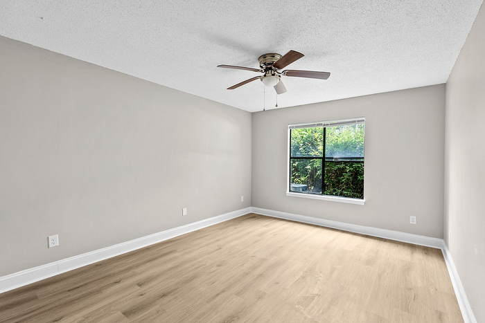 Bright and spacious bedroom with elegant wood flooring, large window view of lush greenery, and modern ceiling fan.